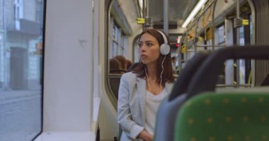Kulaklıklı ciddi bir kızın portresi. Müzik dinlemek için akıllı telefonu kullanıyor. Çekici kadın onu günlük gidip ve müzik dinlerken şehir tramvay pencereyakınında oturma.