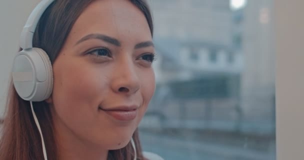 Caucasian young attractive woman listening to the favorite music in the big white headphones while going in the tram or bus. Close up. — Stock Video