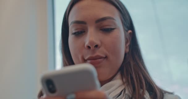 Вид снизу на смартфон в руках молодой кавказки, красивой на вид девушки, пока она постукивает и текстурирует сообщение. Закрыть. — стоковое видео
