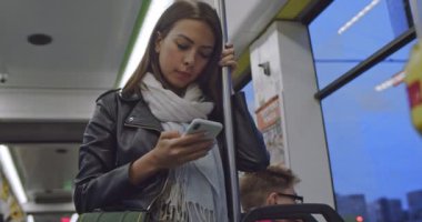 Beyaz tenli, çekici ve şık bir kadın tramvayda duruyor ve elinde tırabzanla akşam saatlerinde telefonda yazı yazıyor..