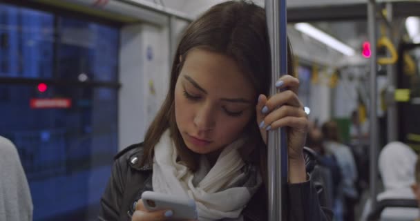 Nahaufnahme der jungen hübschen kaukasischen Frau in stylischem Outfit, die einen Handlauf in der Straßenbahn hält, während sie nach Hause kommt und auf das Smartphone tippt. — Stockvideo