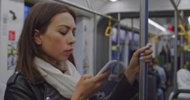 Beyaz, güzel bir kadın tramvayda duruyor ve elinde bir tırabzanla cep telefonuna mesaj yazıyor. Kapat..