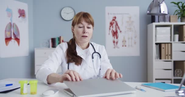 Kaukázusi fáradt doktornő kikapcsolja a számítógépet, miközben az asztalnál ül a szekrényben. Csinos orvos kimerült, miután a laptopon dolgozott a kórházi irodában. Gyógyszer és egészségügy. Orvosi fogalom. — Stock videók