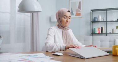 Mutlu Müslüman kadın evdeki bilgisayarını bitirir, bilgisayarını kapatır ve kameraya bakar. Evde çalışmak, kişisel izolasyon uzaktan kumandası Coronavirus krizi konseptinde çalışmak.