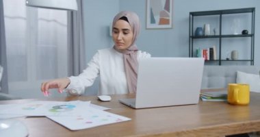 Modern yurt ofisinde dizüstü bilgisayar kullanan güzel Asyalı Müslüman kadın. Küçük işletme sahibi, girişim girişimcisi. Evde çalışmak, kişisel izolasyon uzaktan kumandası Coronavirus krizi konseptinde çalışmak.