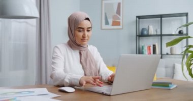 Modern yurt ofisinde dizüstü bilgisayar kullanan güzel Asyalı Müslüman kadın. Küçük işletme sahibi, girişim girişimcisi. Evde çalışmak, kişisel izolasyon uzaktan kumandası Coronavirus krizi konseptinde çalışmak.