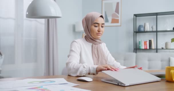 Šťastná muslimka dokončí práci na počítači doma, zavře notebook na pracovišti a podívá se do kamery. Práce doma, samostatná izolace vzdálená práce během konceptu koronavirové krize. — Stock video