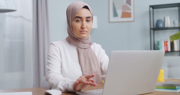 密切关注在笔记本电脑上工作的年轻穆斯林女学生，从计算机上阅读新闻，与网络教师在线学习，解决家里的问题。严肃的女人寻找灵感和想法. — 图库视频影像