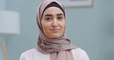 Kendine güvenen, tesettürlü genç müslüman kadının ofis kamerasına bakışını kapat. Beyaz dişli, güzel yüzlü, kapalı mekan portresi için poz veren mutlu milenyum gündelik profesyonel bayan..