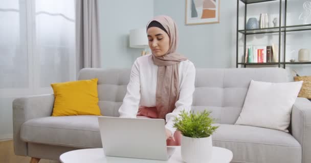 Middle plan of young concerned muslim student girl working on laptop computer, μελέτη σε απευθείας σύνδεση με το Διαδίκτυο δάσκαλος, σκέψης επίλυση του προβλήματος στο σπίτι. Σοβαρή αναζήτηση γυναικών για έμπνευση και ιδέες. — Αρχείο Βίντεο