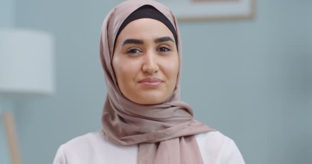 自信を持って笑顔の若いイスラム教徒の女性のヒジャーブの自宅のオフィスでカメラを見て閉じます。幸せな千年カジュアルプロ女性とともに白い歯可愛いです顔ポージングのために閉じますアップポートレート屋内. — ストック動画