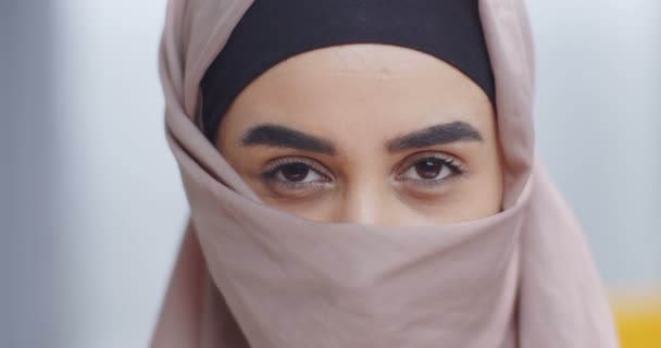 Nahaufnahme Porträt einer schönen muslimischen Frau im Hidschab, die ihr Gesicht mit einem Taschentuch verhüllt. Geheimnisvoller Anblick. Muslimische Frau im Kopftuch-Hijab. Junges Mädchen mit Augen Make-up Blick in die Kamera. — Stockvideo