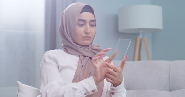 Närbild porträtt muslimsk kvinna i hijab med hjälp av en futuristisk glas telefon teknik i moderna vardagsrum, internet mobil display telefon, modern innovation koncept. — Stockvideo