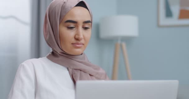Retrato de una joven estudiante musulmana preocupada que usa hijab trabajando en una computadora portátil, estudia en línea con un profesor de Internet, resolviendo problemas en casa. Mujer seria búsqueda de inspiración e ideas . — Vídeos de Stock