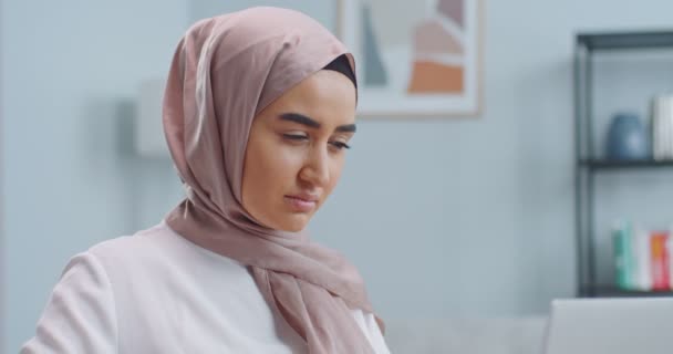 El primer plano de la mujer joven hermosa musulmana en el hiyab se pone las gafas y comienza a trabajar. Estudiante escribiendo en el ordenador usando gafas. Trabajo remoto, estudio en línea, concepto de oficina en casa . — Vídeos de Stock