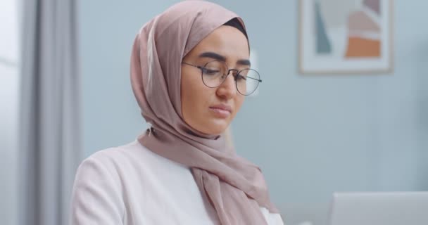 Genç ve güzel Müslüman kadın tesettürlü gözlüğünü çıkarırken işini bitir ve kameraya bak. Öğrenci bilgisayarda gözlük kullanarak daktilo kullanıyor. Uzak çalışma, çevrimiçi konsept eğitimi. — Stok video