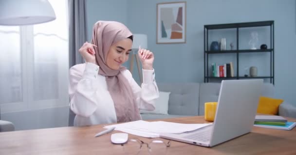 Plan medio de feliz joven musulmán joven bailando con alegría después de obtener una excelente calificación para el examen. Chica celebrando la competencia ganadora. Mujer feliz sentada en la mesa estudiando en casa oficina . — Vídeos de Stock