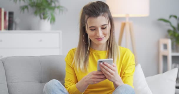 Portræt af glad kvinde nyder at søge på mobiltelefon i hjemmekontoret. Overrasket dame surfing på internettet på telefonen i lejlighed. Glædelig pige læser gode nyheder på telefonen i slowmotion. – Stock-video