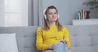 Güzel, genç bir kadın, beyaz, rahat kulaklıklarla telefondan müzik dinliyor. Kulaklıkla meditasyon yapan kız. Kişisel gelişim kavramı, evde dinlenme, boş zaman..