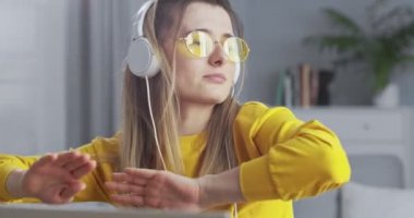 Sarı güneş gözlüklü küstah sarışın beyaz kulaklıklı müzik dinliyor ve modern şık oturma odasında kanepenin yanında dans ediyor. Kız evde kalırken eğleniyor..