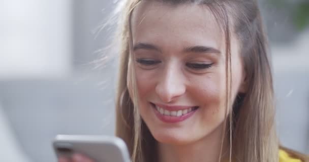 美丽的金发姑娘在手机上看到短信，面带微笑，在智能手机屏幕上看起来很满意。现代生活、交流、关系、生活方式的概念. — 图库视频影像