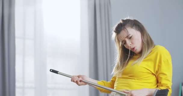 Close up front portrait of happy young blonde woman washing floor with plastic mop. Playful girl singing and dancing, pretending playing at guitar. People and technology concept. — Stock Video