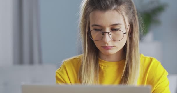 Schlaue Studentin mit Brille, die am Computer arbeitet und zu Hause auf einer bequemen Couch sitzt. Das Konzept von Online-Lernen, Arbeiten zu Hause und Lebensstil. — Stockvideo