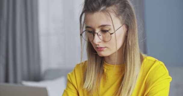 Mujer joven y segura que trabaja en una computadora, revisa el correo electrónico y responde en línea. La chica terminando de trabajar y ajustando las gafas, sonriendo felizmente y mirando a la cámara . — Vídeo de stock