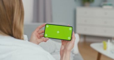 Yeşil ekranlı ve takip hareketli siyah yatay telefonlu peçeteli hasta kadının omzunun üstünden bakın. Grip olmuş bir kız evde oturuyor, burnunu siliyor ve web kamerasıyla görüntülü sohbet ediyor..