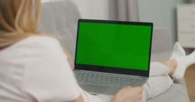 Yeşil ekranlı dizüstü bilgisayarı olan bir kadının omzunun üstünden bak. Kız kendini izole ederek evde oturuyor, video izliyor ve bilgisayar kamerasından sohbet ediyor. Videochat. Krom anahtar.
