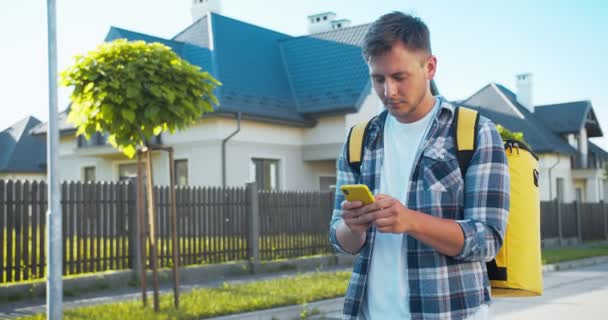 Joven mensajero caucásico caminando por la calle en busca de la casa de los clientes. Hombre adulto guapo utilizando mapas en el teléfono inteligente, en busca de la dirección. Entrega, servicio de compras . — Vídeos de Stock