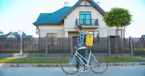 Homem caucasiano atraente do serviço de entrega com mochila e bicicleta andando pela rua. Bonito jovem procurando em mapas e procurando o endereço do cliente. Compras e entrega . — Vídeo de Stock