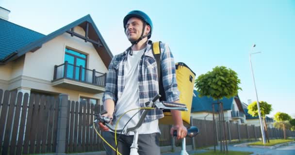 Joyful jovem mensageiro masculino com um backback térmico do serviço de entrega. Bonito caucasiano com bicicleta de pé na rua, olhando e sorrindo para a câmera. Entrega e compras . — Vídeo de Stock