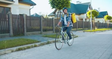 Siparişi ulaştırmak için bisikletle caddeye çıkan yakışıklı beyaz kurye. Kasklı ve termal çantalı mutlu teslimatçı. Güvenli alışveriş ve teslimat..