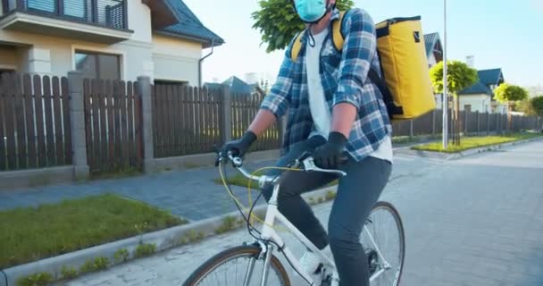 白人男性の宅配業者が自転車に乗って通りまで注文を配達します。ヘルメットとお客様の住所を探している熱バックパック付きの幸せな若い配達人。遠くの購入オンライン. — ストック動画