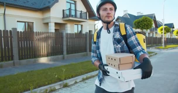 Young Caucasian male from delivery service walking down the street in medical mask. Delivery guy holding cardboard boxes with food, pizza from restaurant in rubber gloves. Coronavirus, pandemic. — Stock Video