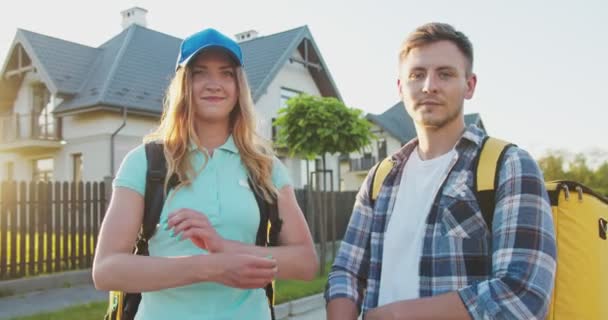 Aantrekkelijke Kaukasische koeriers met thermische rugzakken die voedsel aan klanten leveren. Gelukkige bezorgers kruisen hand over borst en glimlachen naar de camera. Leveringsservice, online winkelen. — Stockvideo