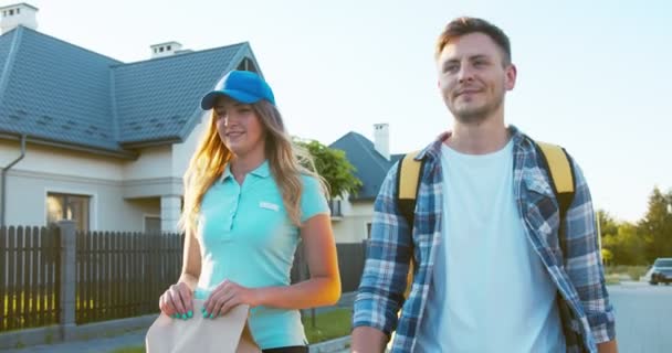 Correios felizes para homens e mulheres que entregam comida. Um tipo bonito com um backback térmico e uma mulher bonita com um paperback a andar e mais cinco. E-commerce, compras online . — Vídeo de Stock