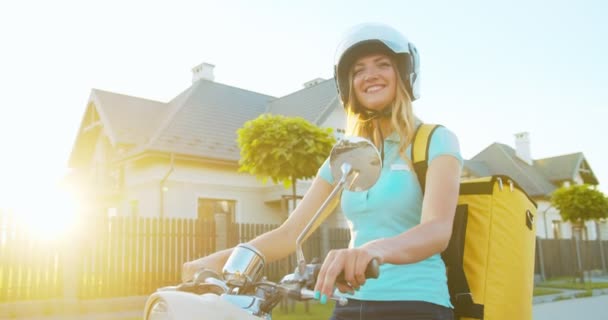 Beautiful young Caucasian woman in safety helmet delivering food, groceries from supermarket. Attractive female courier sitting on a scooter, looking and smiling at camera. Online shopping, purchase. — Stock Video