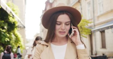 Güneşli bir günde sokakta yürürken ön planda cep telefonuyla sohbet eden şapkalı güzel beyaz kızın portresini yakından çek. Arka planda gülümseyen neşeli melez kadınlar. Çağrı kavramı