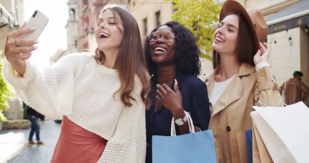 Mixed-Rennen glückliche Frauen posieren im Freien. Hübsches kaukasisches Mädchen macht Selfie-Videos auf dem Smartphone, während es mit Freunden in der Stadt steht.Porträt einer Afroamerikanerin, die mit der Hand in die Handykamera winkt — Stockvideo