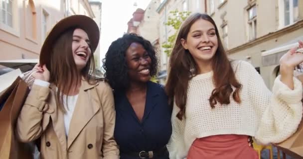 Gelukkige multi-etnische diverse vrouwen wandelen in de stad in het zonlicht. Portret van mooie lachende vrouwen met boodschappentassen. Afro-Amerikaanse en blanke meisjes praten buiten. Emoties concept — Stockvideo