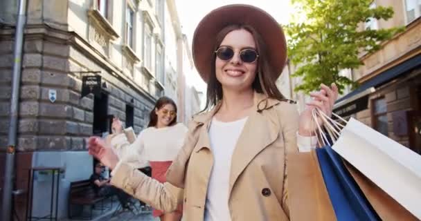 Щасливі багатоетнічні дівчата в сонцезахисних окулярах з торговими сумками, що ходять по вулиці. Портрет радісних кавказьких гарних жінок, які розважаються в місті. Афроамериканська дівчина посміхається надворі. Концепція покупки — стокове відео