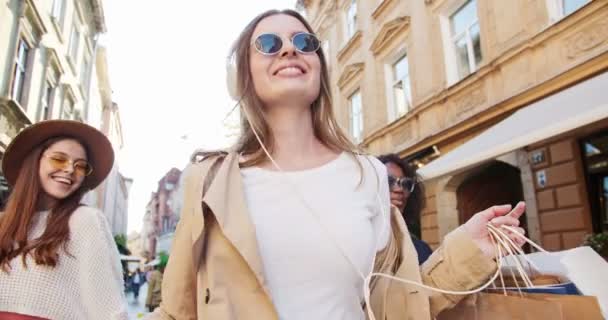 Mooie vrolijke gemengde ras jonge vrouwen lopen op straat en houden boodschappentassen. Vrolijk blank meisje met een zonnebril in een goed humeur. Portret van Afro-Amerikaanse vrouw in zonlicht. Shopper concept — Stockvideo