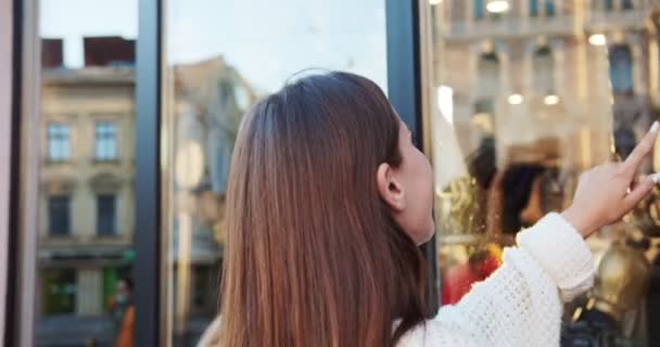 Schöne kaukasische glückliche Mädchen, die auf der Straße in der Stadt stehen und die Vitrine betrachten. Nahaufnahme Porträt einer hübschen fröhlichen Frau, die auf Schaufensterpuppen im Schaufenster zeigt und draußen lächelt. Spaßkonzept — Stockvideo