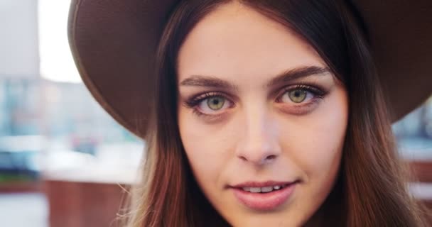 Primer plano retrato de niña bonita alegre en sombrero mirando hacia otro lado y sonriendo a la cámara al aire libre. Alegre hermosa mujer joven caucásica con la cara feliz de pie en la calle de la ciudad. Concepto de emociones — Vídeos de Stock