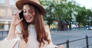 Şapkalı neşeli kız sokakta durup akıllı telefondan konuştuktan sonra alışverişlerden memnun. Kasabada cep telefonuyla konuşan güzel mutlu beyaz kadın portresi. Çağrı kavramı