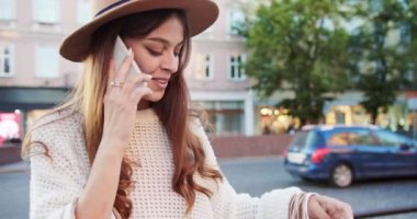 Sokakta durup akıllı telefondan sohbet ettikten sonra alışveriş yapan şapkalı neşeli bir kız. Şehirde cep telefonundan arayan güzel, mutlu, beyaz bir kadının portresi. Konuşma konsepti