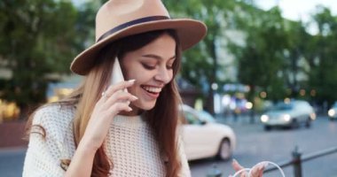 Açık havada durup akıllı telefondan konuşurken şapkalı güzel bir kızın portresini yakın mesafeden çek. Cep telefonundan alışveriş yaptıktan sonra güzel, mutlu bir beyaz kadın. Konuşma konsepti