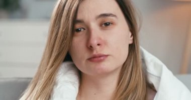 Oturma odasındaki kanepede battaniyenin altında oturup peçeteye sümküren, gripli, beyaz, genç bir kızı yakından çek. Coronavirüs belirtileri gösteren hasta bir kadın..